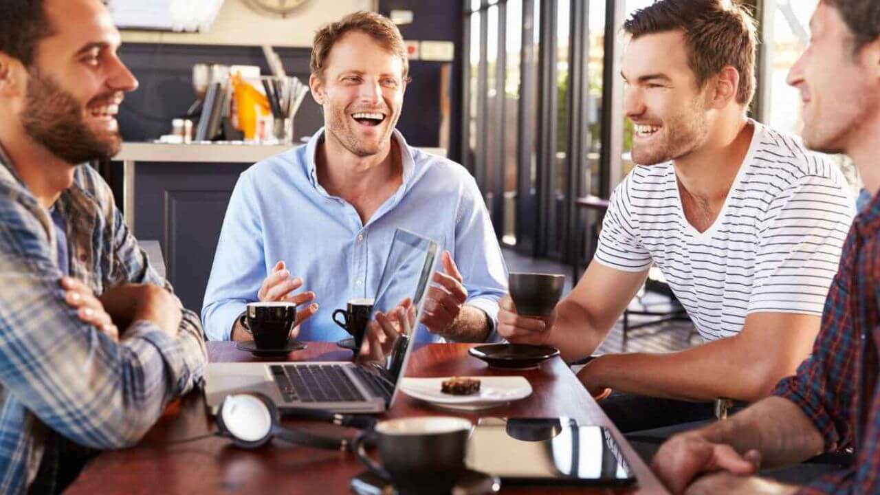 Group of Men Sitting at a Table With Coffee Cups and Laptops