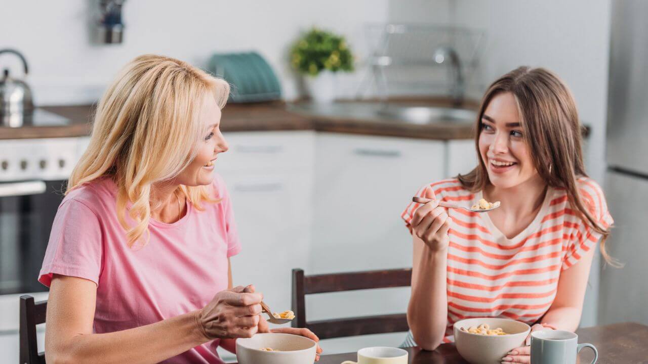 Happy Mother and Daughter Talking While Sitting in the Kitchen Eating Cereals