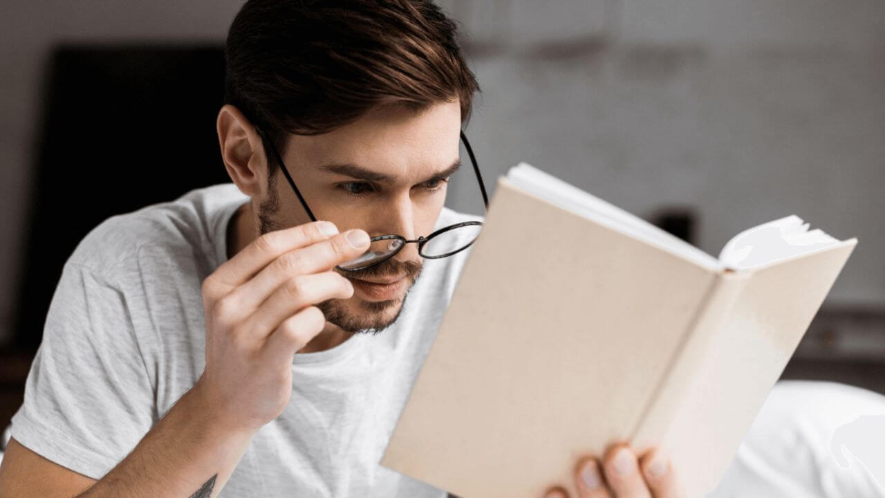 Man Holding His Glasses and Looking at a Book