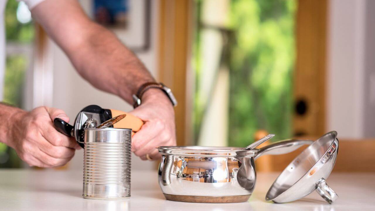 Man Opening Can with Can Opener in Kitchen