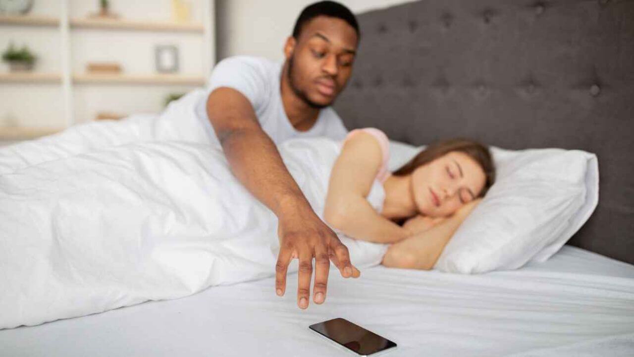 Man Reaching the Phone of His Partner While She Is Sleeping