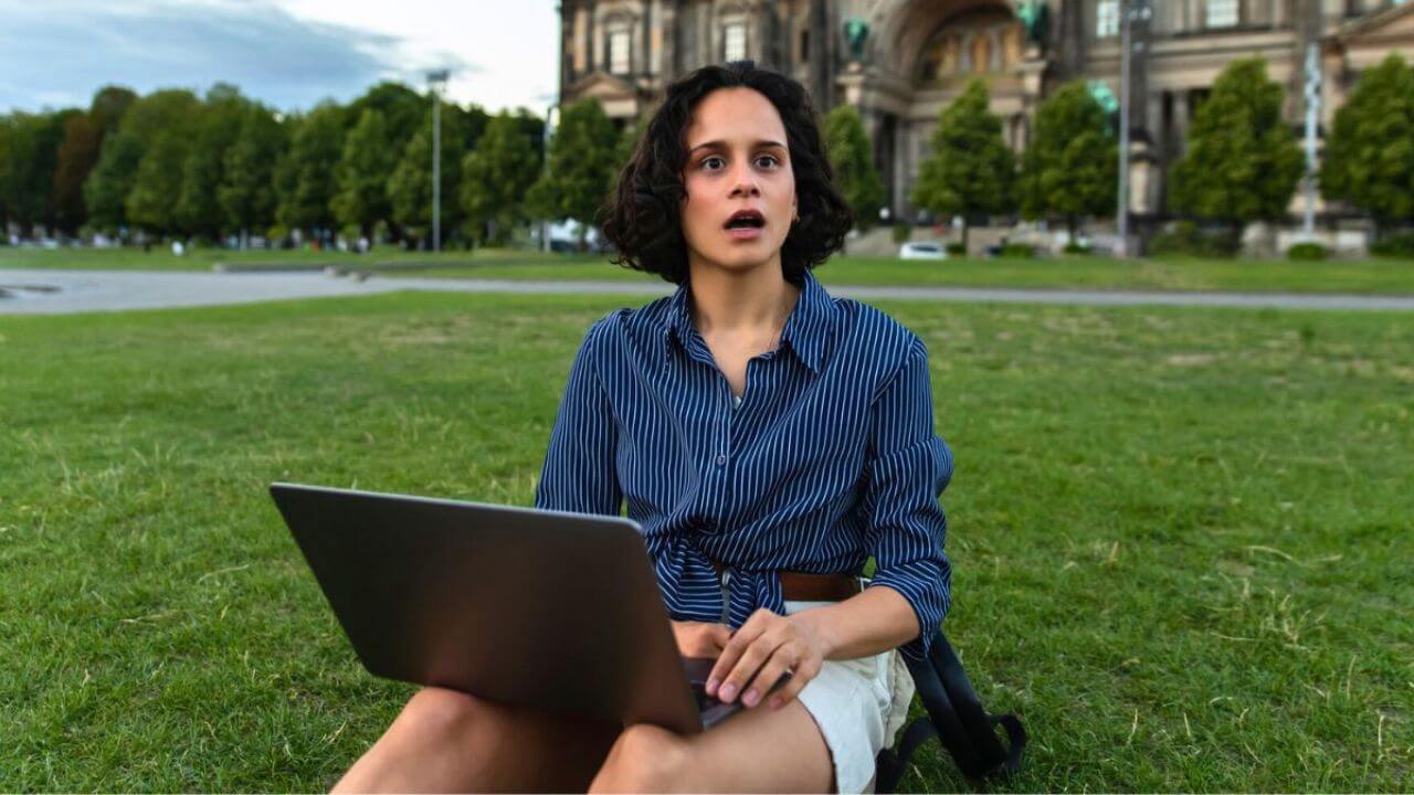 Shocked Young Woman Holding Laptop and Sitting on Grass