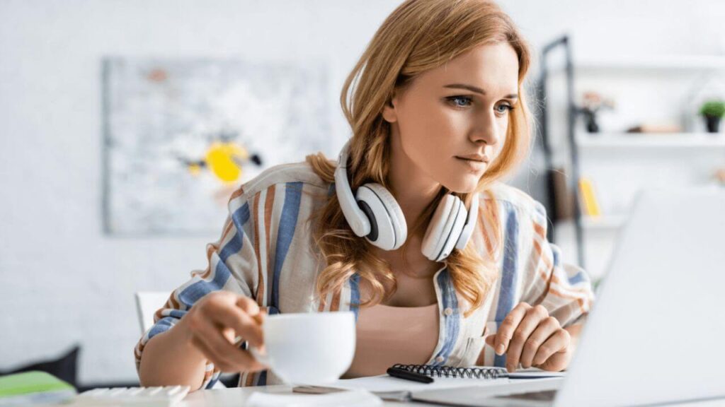 Woman Holding Cup and Working with Laptop