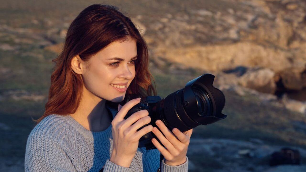 Woman Outside Holding A DSLR Camera Smiling Looking At The Side